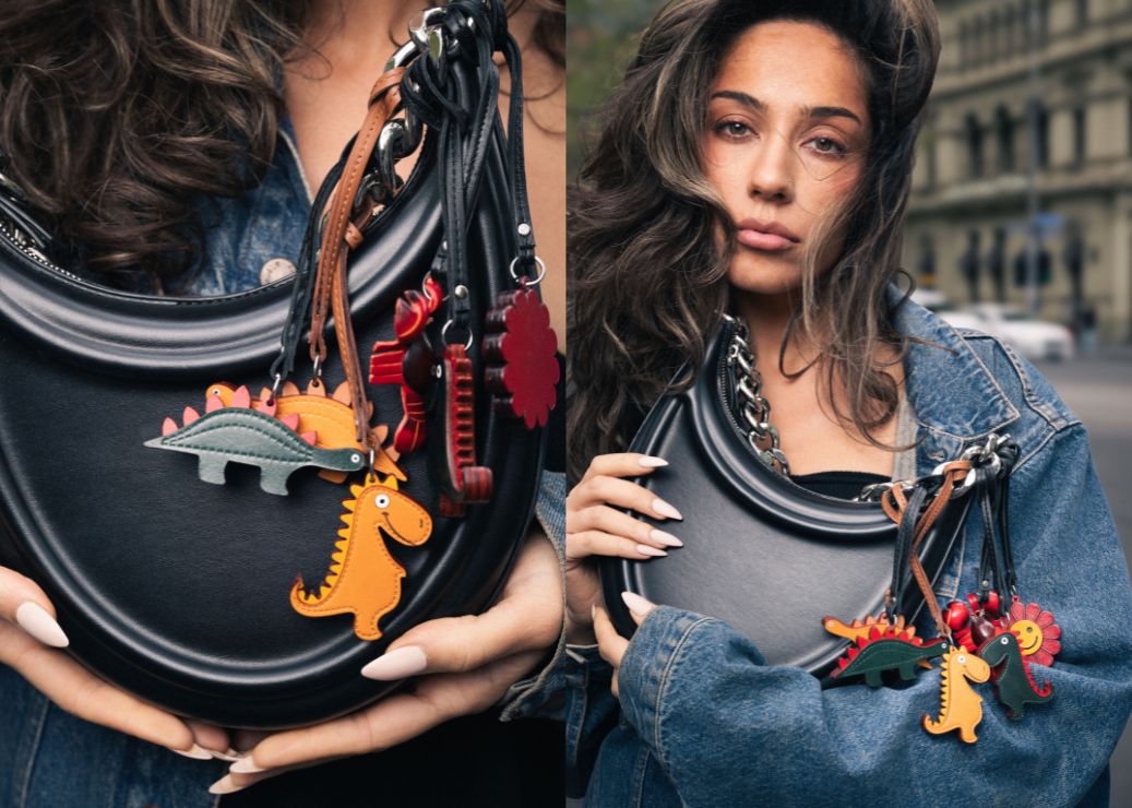 Person holding a black handbag with colorful dinosaur charms, with a city street in the background.