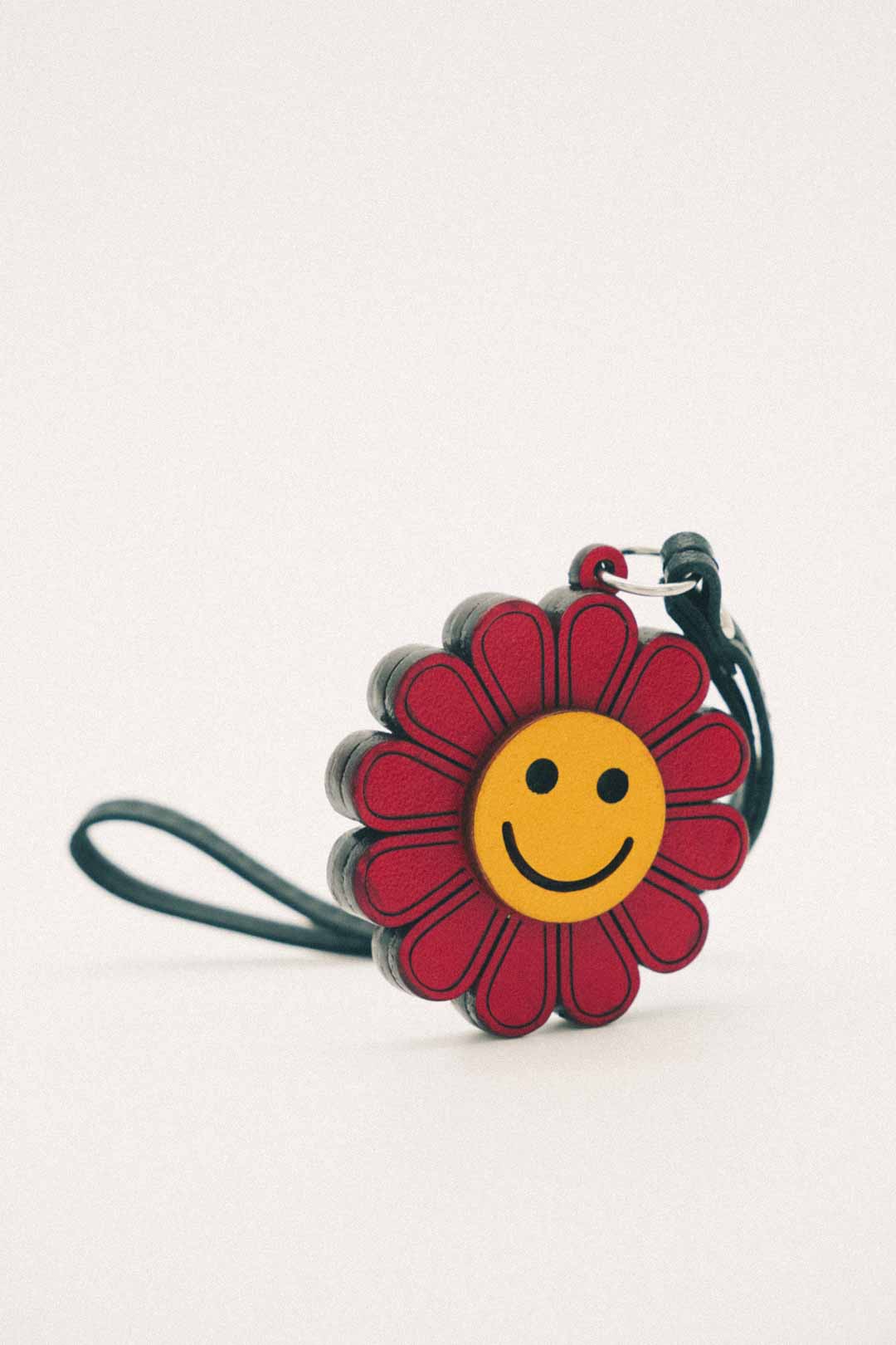 Red and yellow flower-shaped handmade leather bag charm with a smiley face on a white background