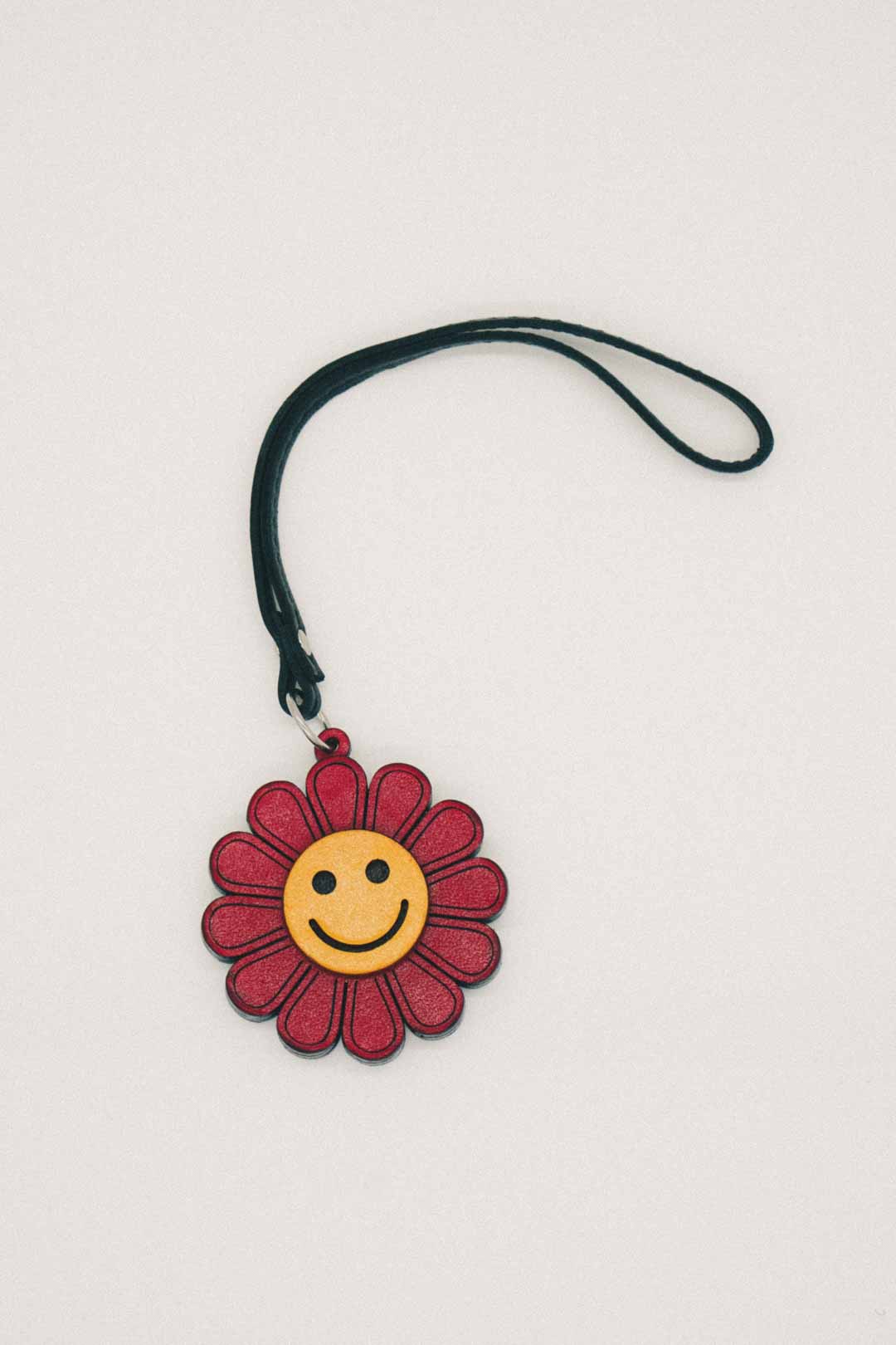 Keychain with a red flower and yellow smiley face on a beige background