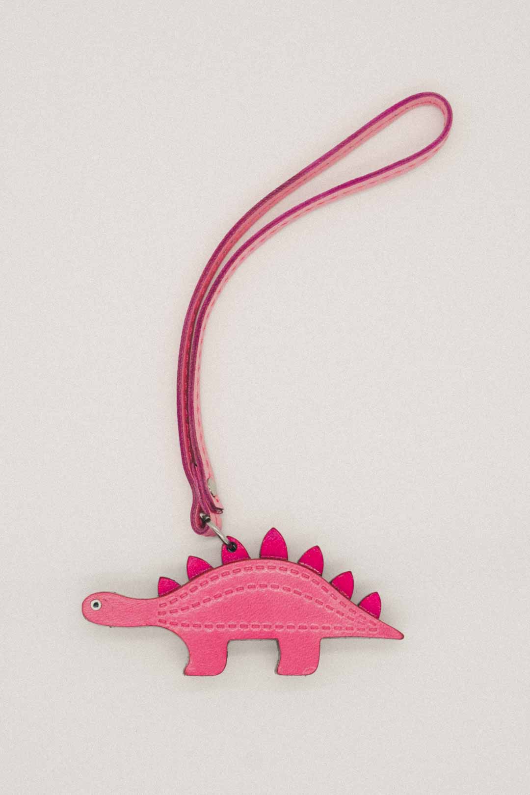 Pink dinosaur-shaped keychain with a strap on a light gray background