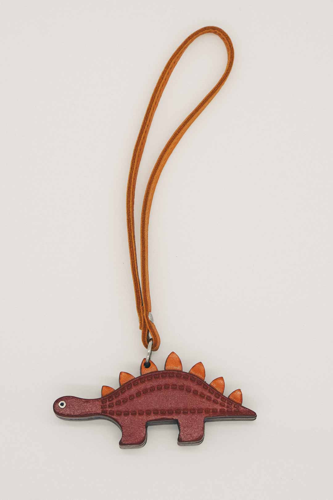 Dinosaur-shaped handmade leather bag charm with a brown strap on a light gray background