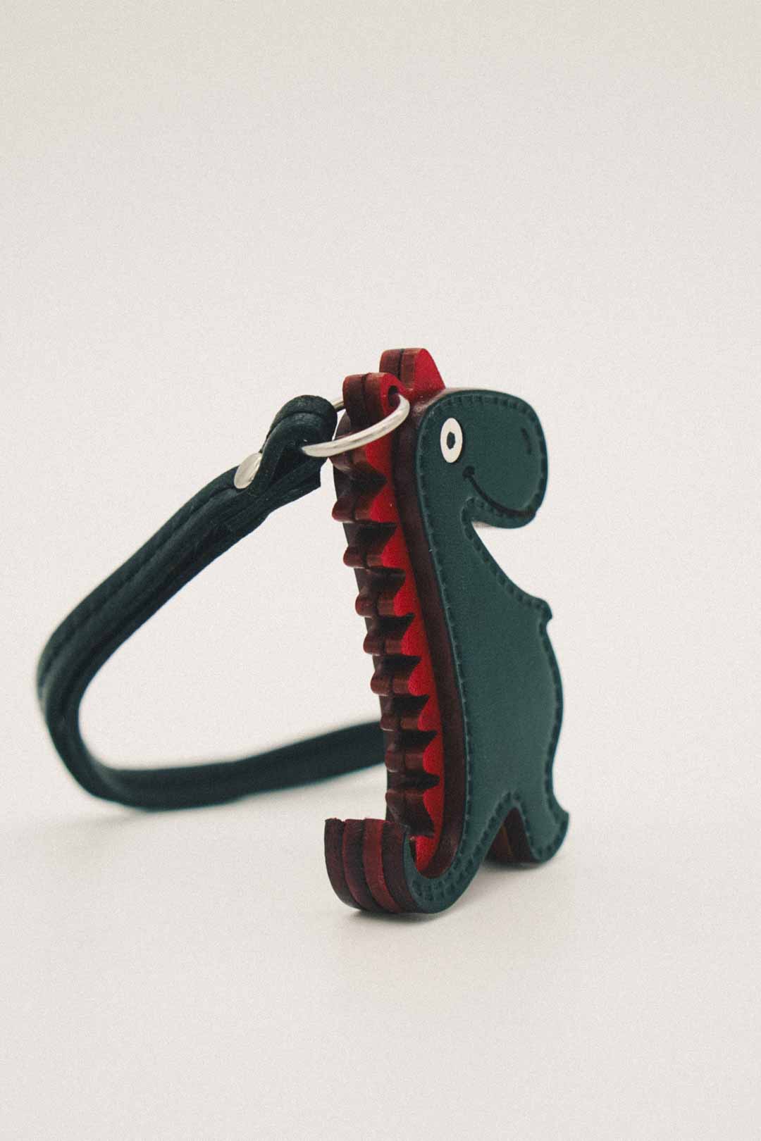 Dinosaur-shaped handmade leather bag charm with red spikes on a white background