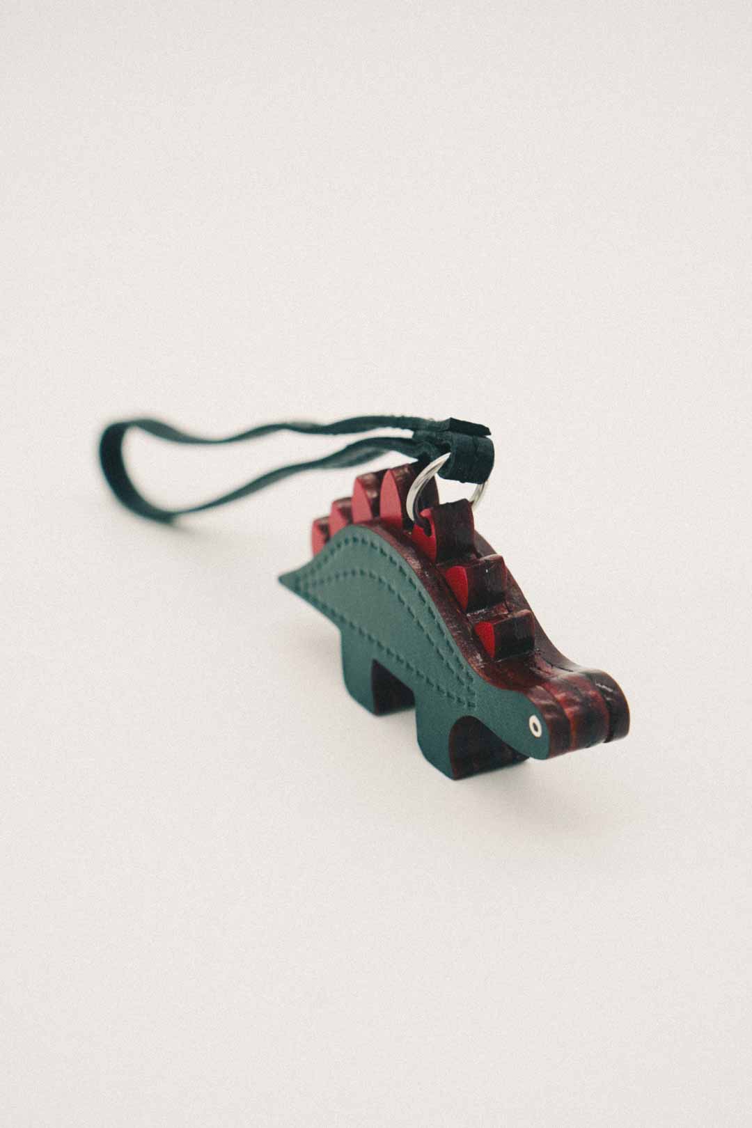 Dark green and red dinosaur-shaped handmade leather bag charm on a white background