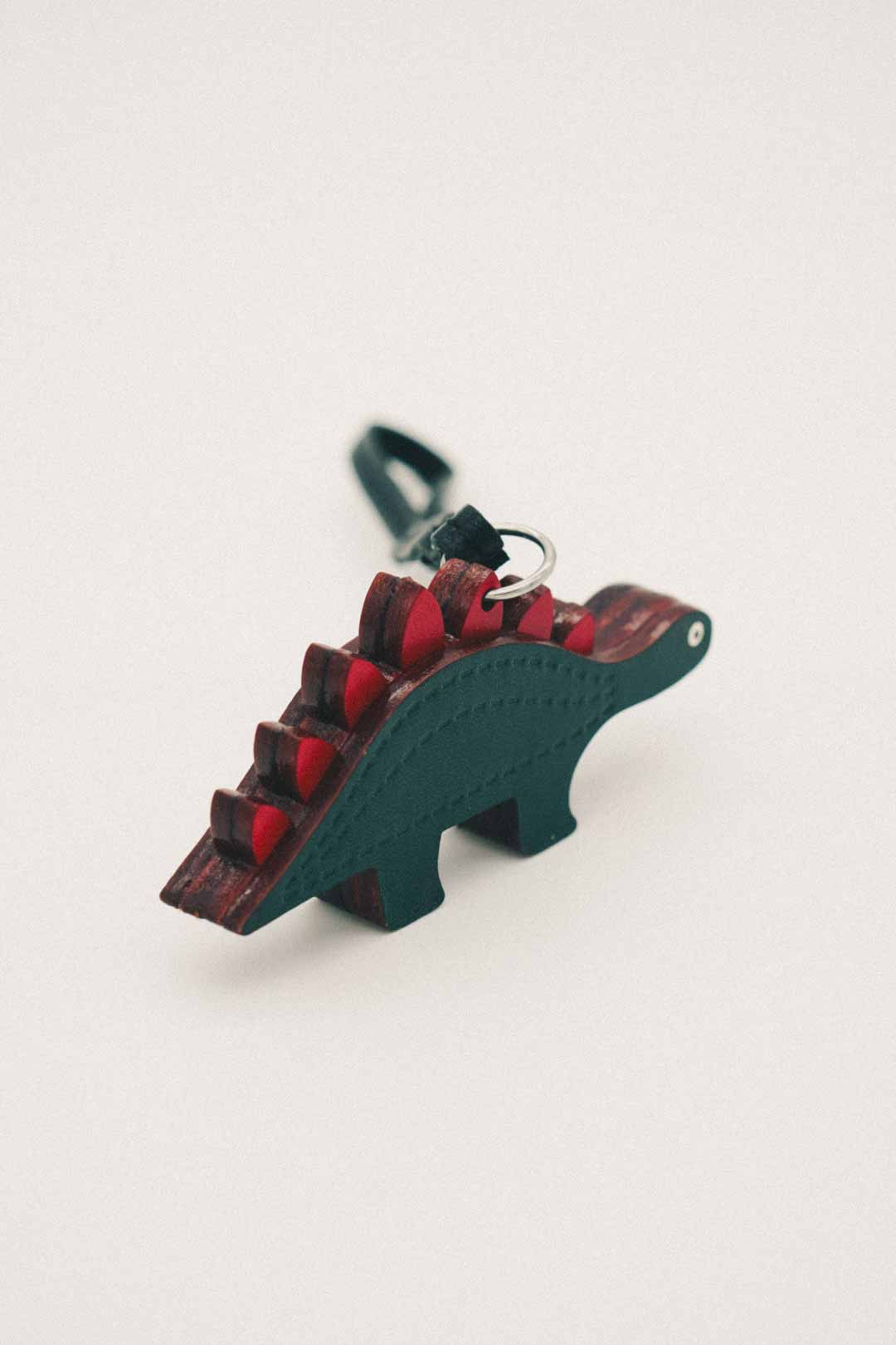 Dark green dinosaur-shaped keychain with red spikes on a white background