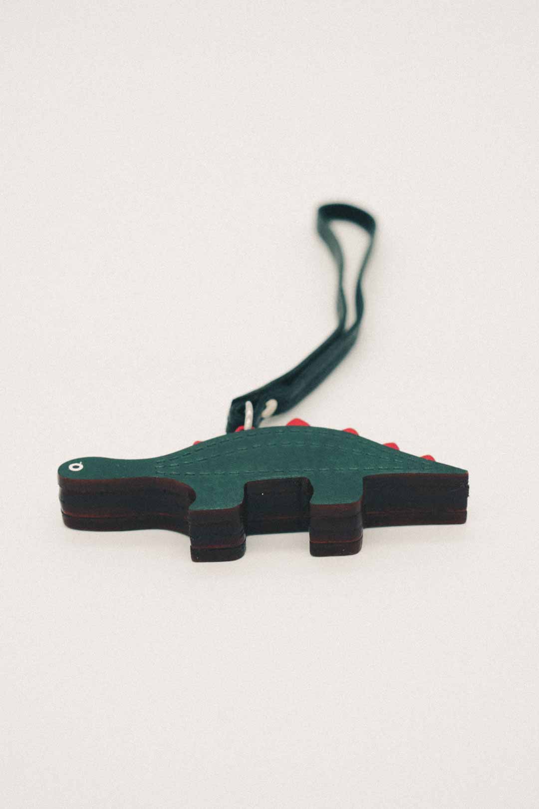 Dark green dinosaur-shaped handmade leather bag charm with a strap on a white background