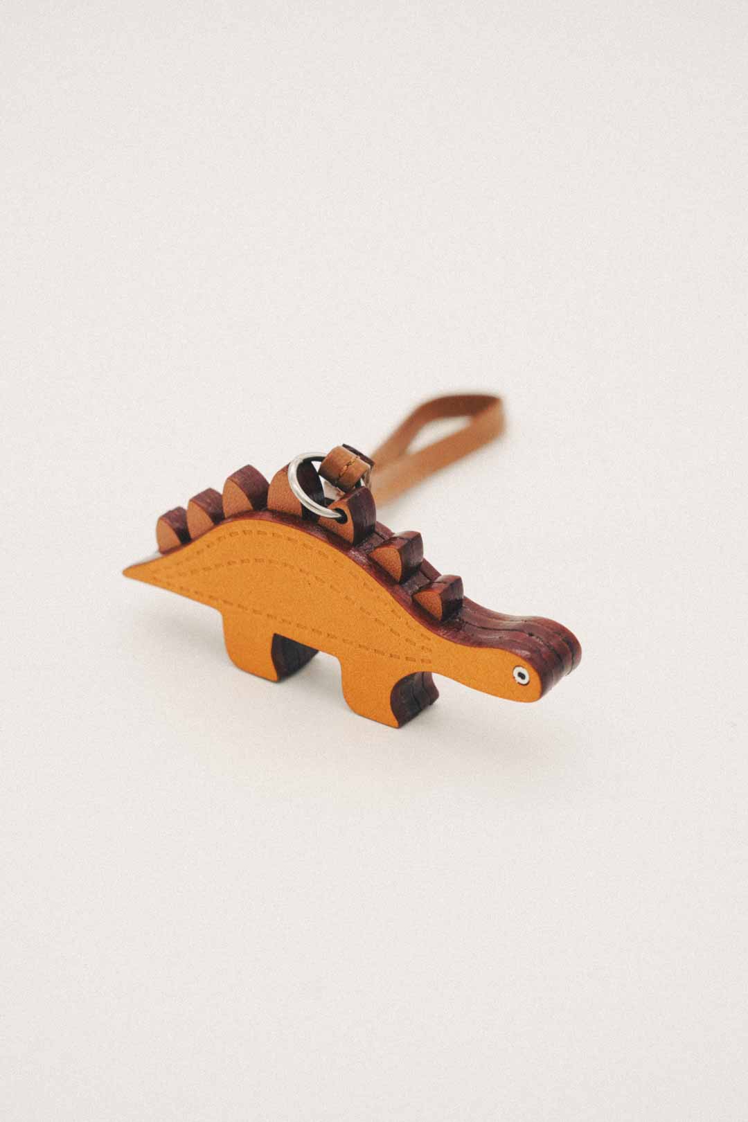 Dinosaur-shaped handmade leather bag charm with brown and orange colors on a white background