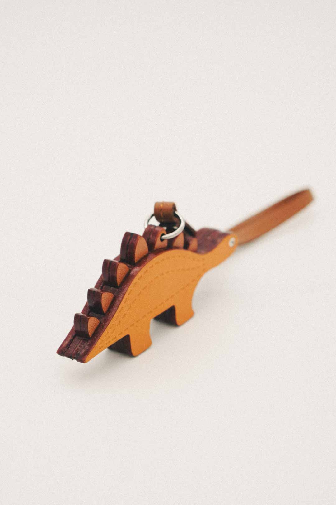 Golden orange dinosaur shaped handmade leather bag charm with spikes and stainless steel ring on white background