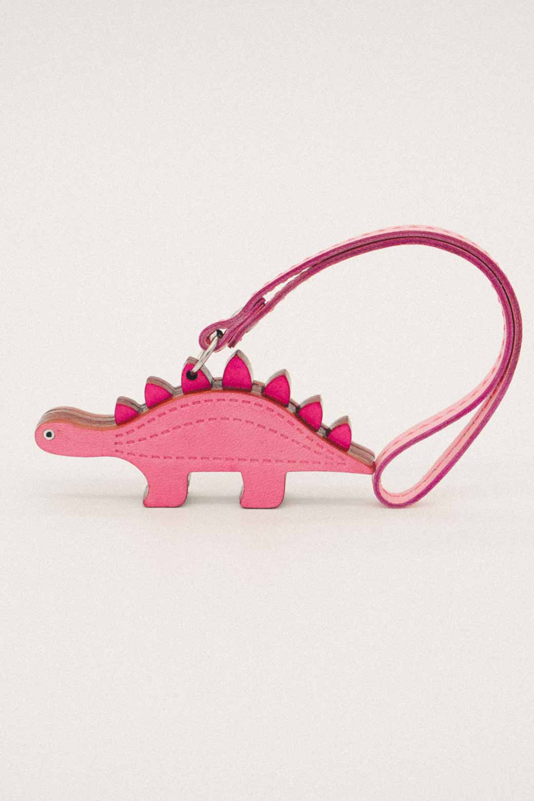 Pink dinosaur-shaped handmade leather bag charm with a strap on a white background