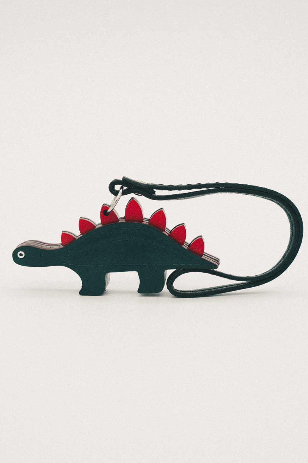 Dark green dinosaur-shaped handmade leather bag charm with red spikes on a white background