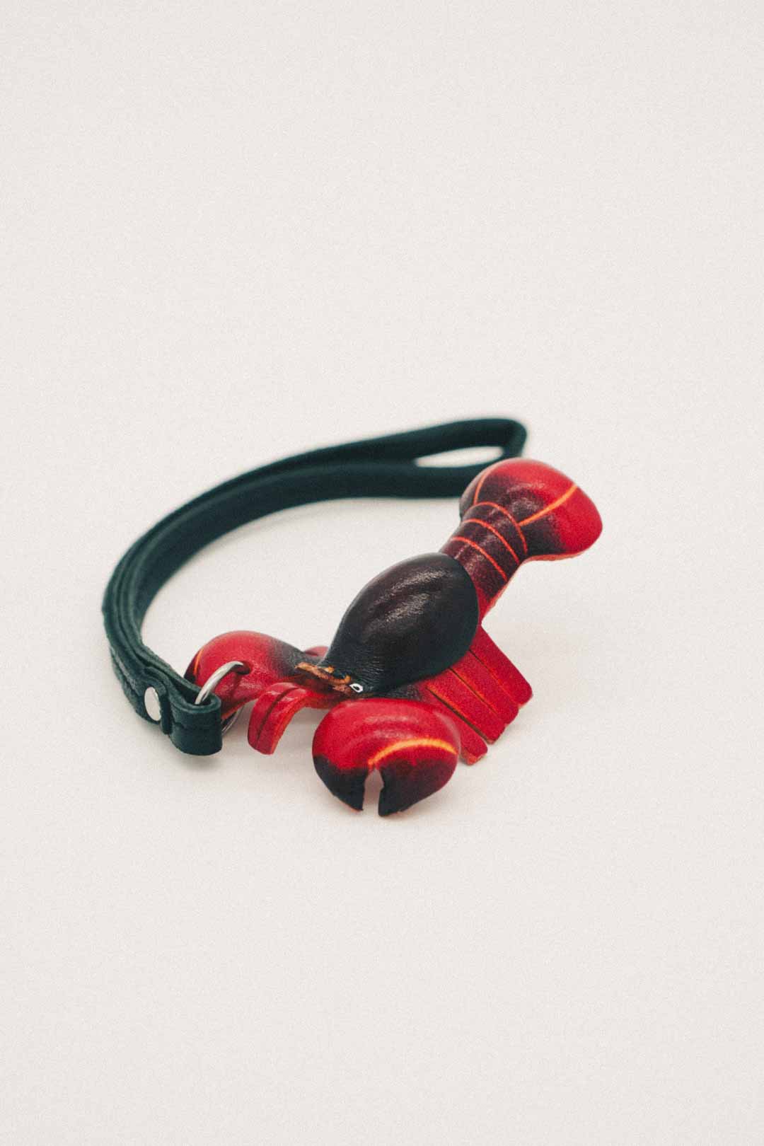 Red and black lobster-shaped handmade leather bag charm with a black strap on a light gray background