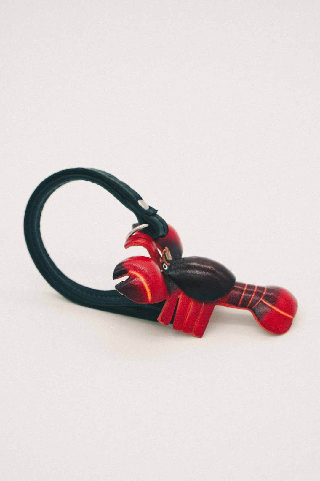 Side view of a lobster-shaped handmade leather bag charm with red and black design on a white background