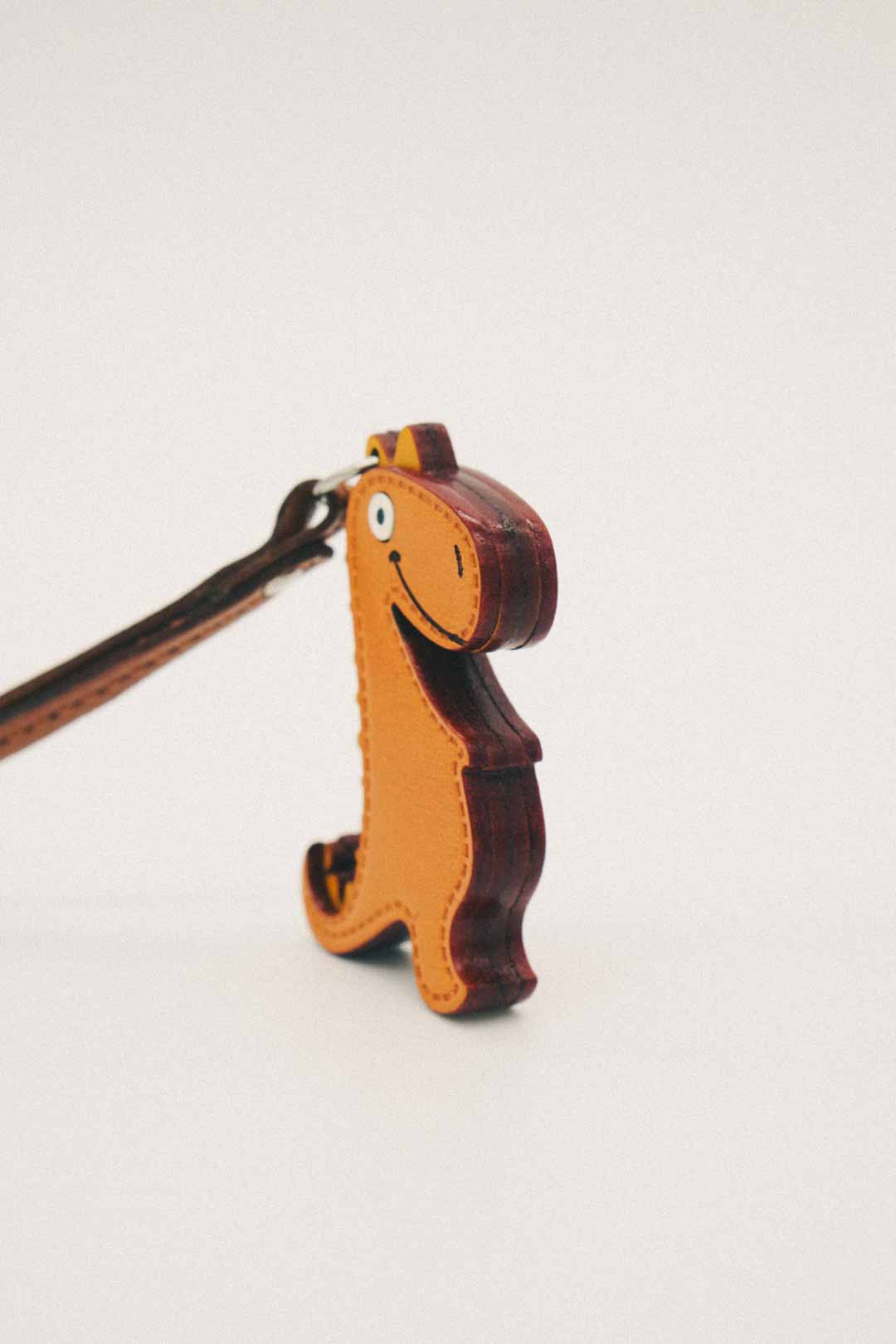 Side view of a handmade leather bag charm shaped like a dinosaur on a white background
