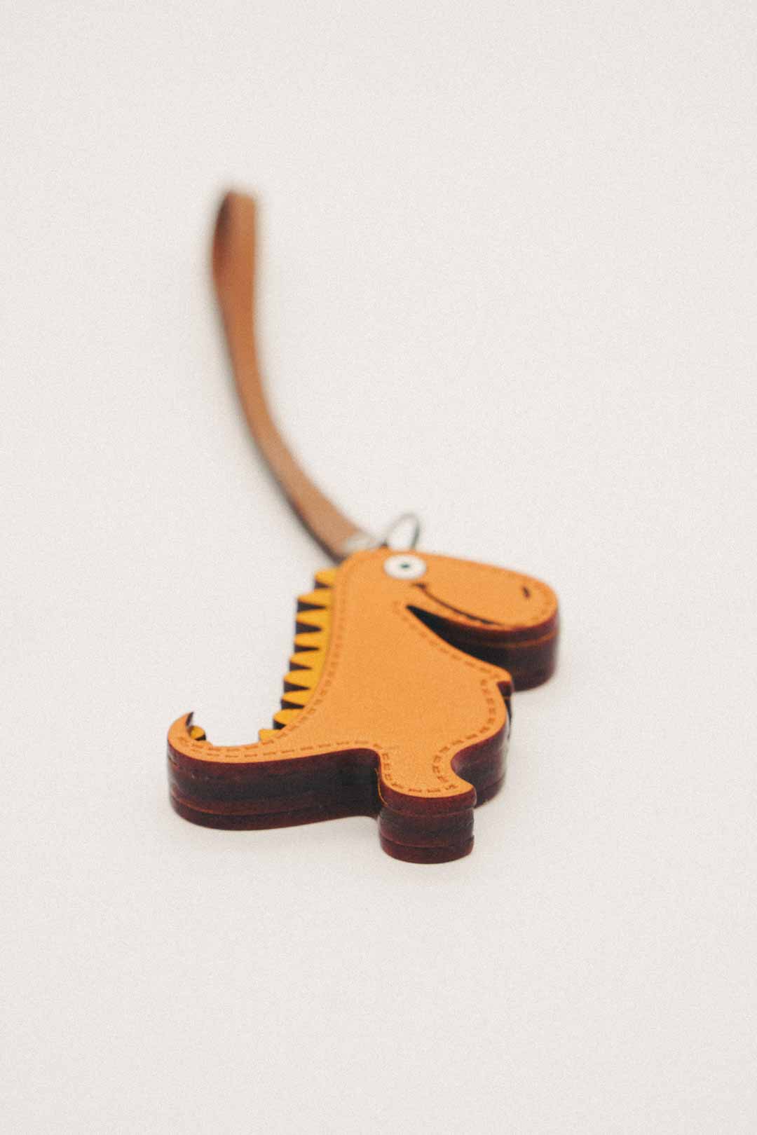 Dinosaur-shaped handmade leather bag charm on a white background
