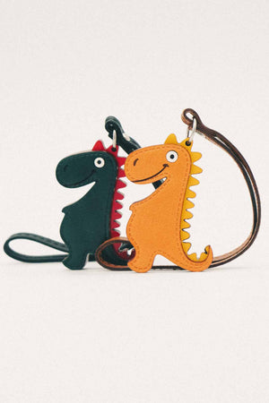 Two dinosaur-shaped handmade leather bag charms, one golden orange and one dark green, on a white background.