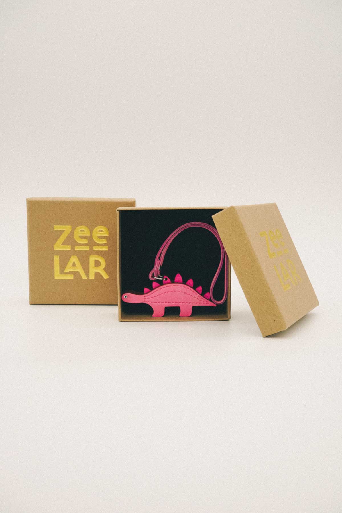Pink dinosaur handmade leather bag charm in a Zeelar box on a white background