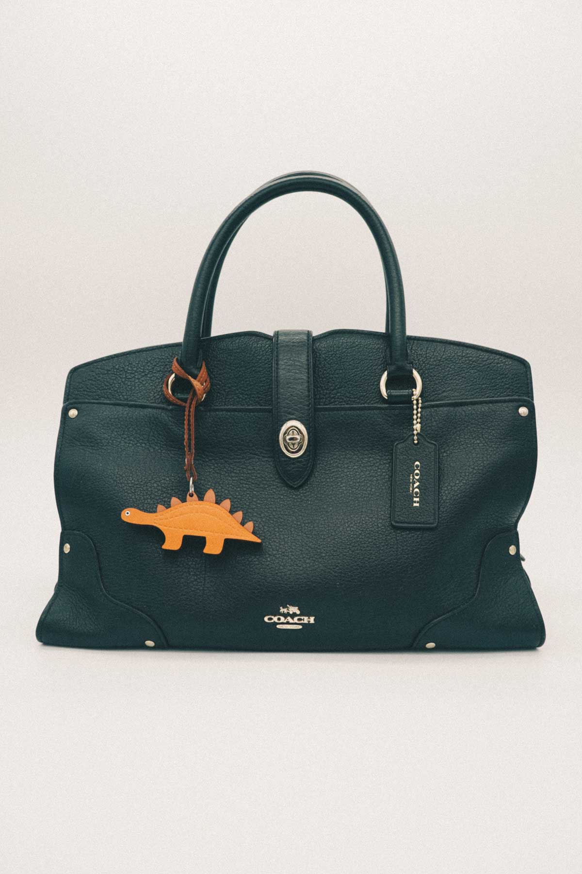 Green handbag with a dinosaur handmade leather bag charm on a white background