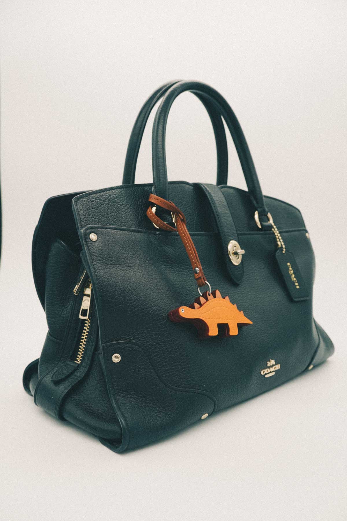 Black handbag with a light brown dinosaur handmade leather bag charm on a white background