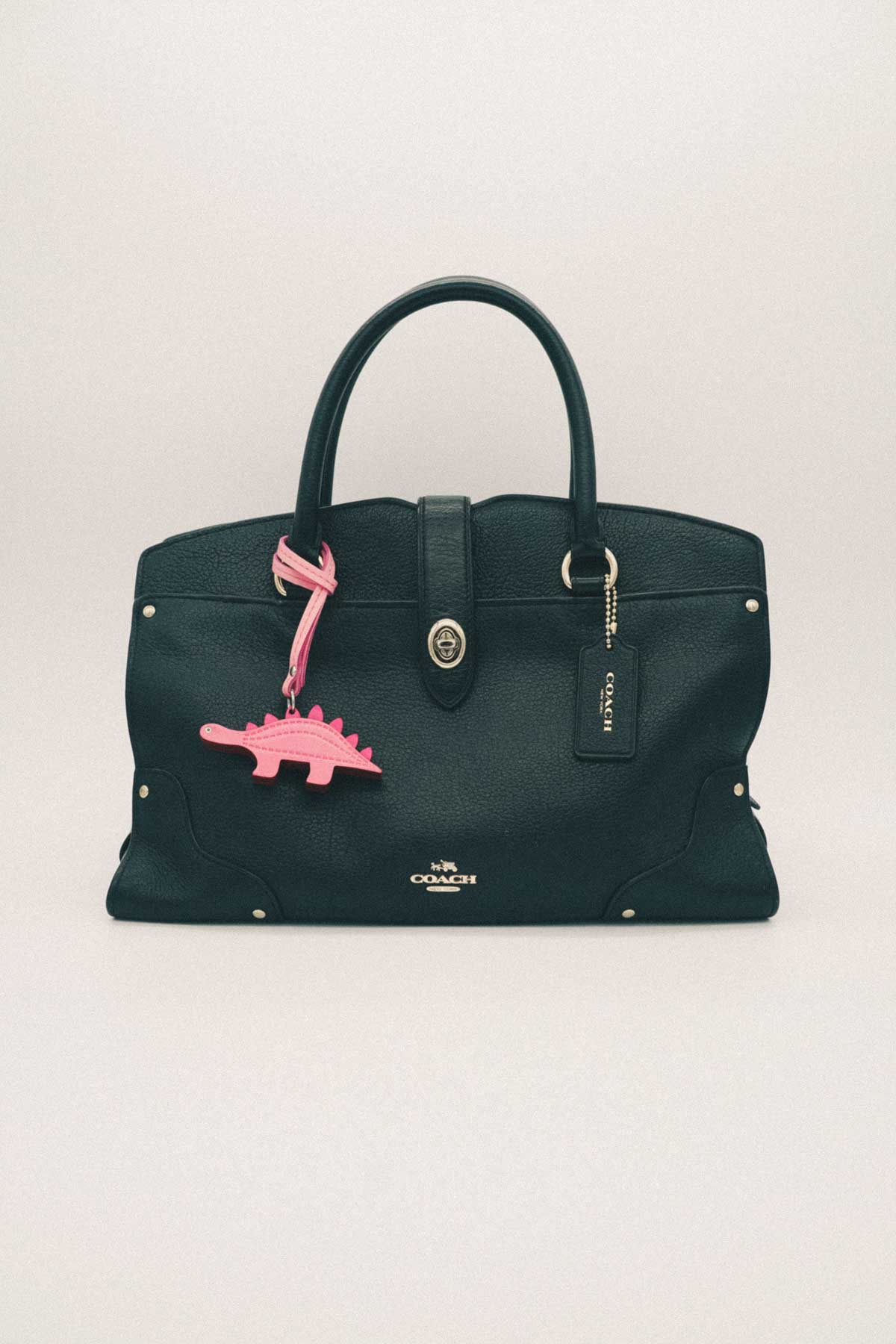 Green handbag with pink dinosaur charm on a white background