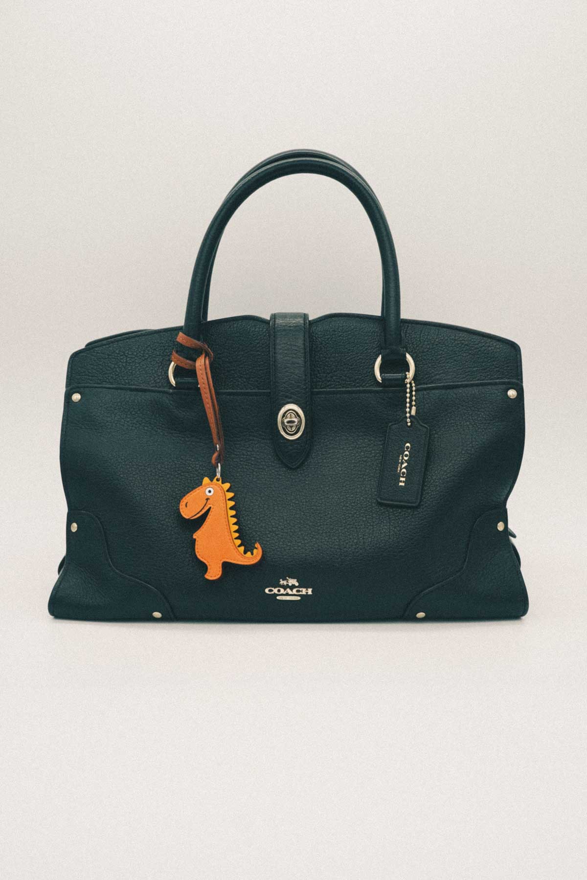 Black handbag with a dinosaur handmade leather bag charm on a white background