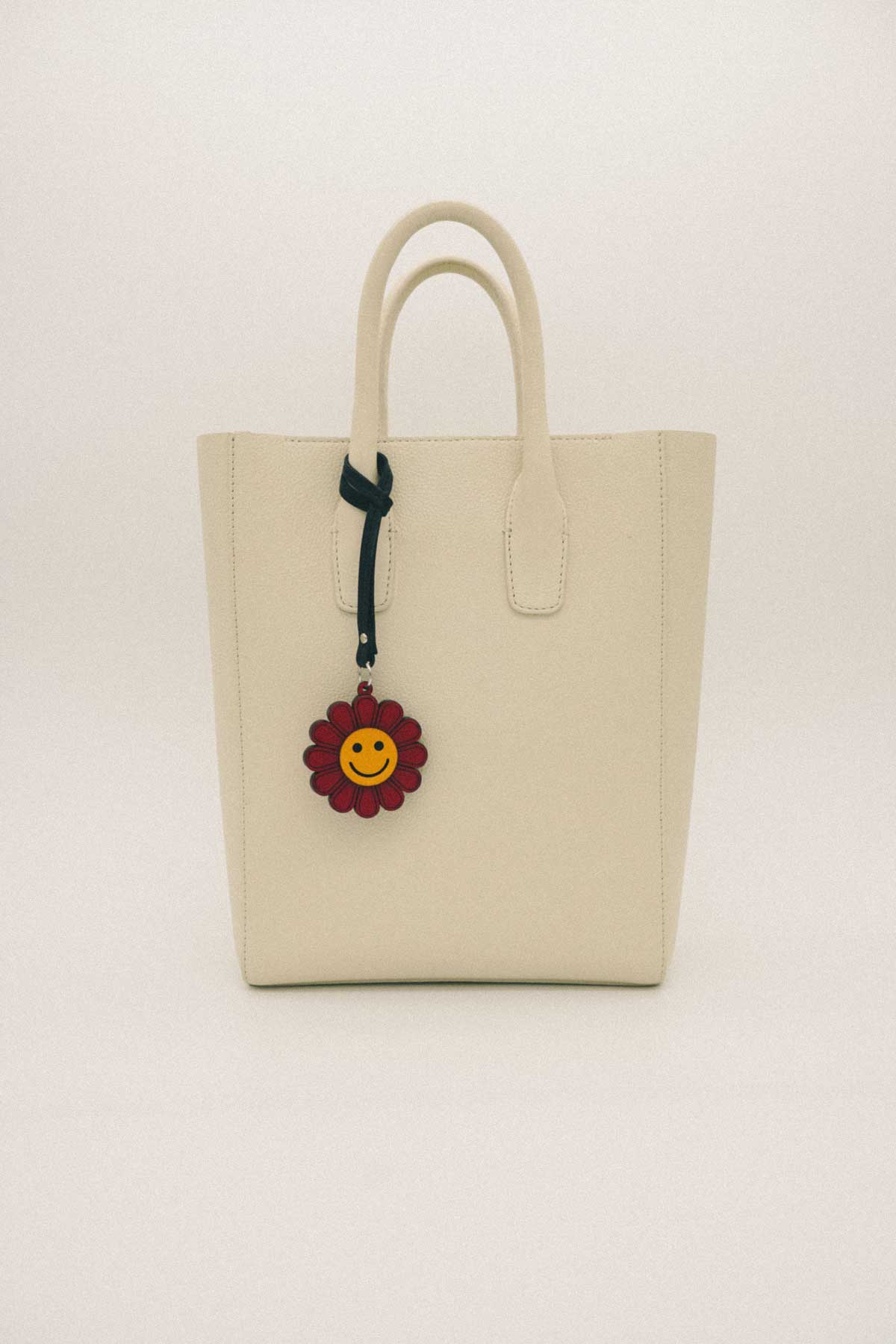 Beige tote bag with a sunflower-shaped charm on a white background