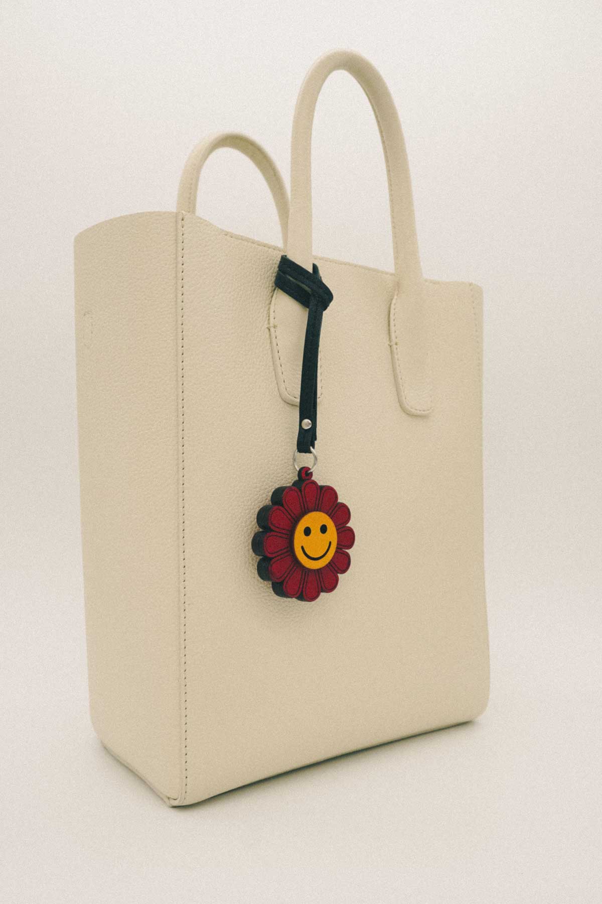 Beige tote bag with a floral charm featuring a smiley face on a white background