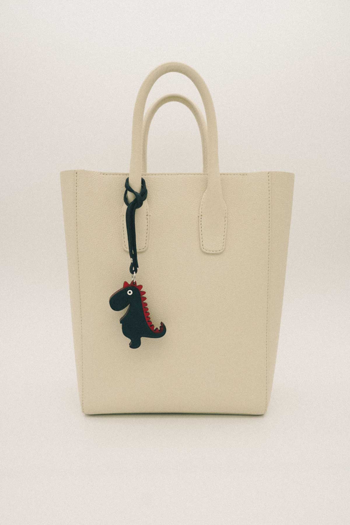 Beige tote bag with a dinosaur handmade leather bag charm on a white background