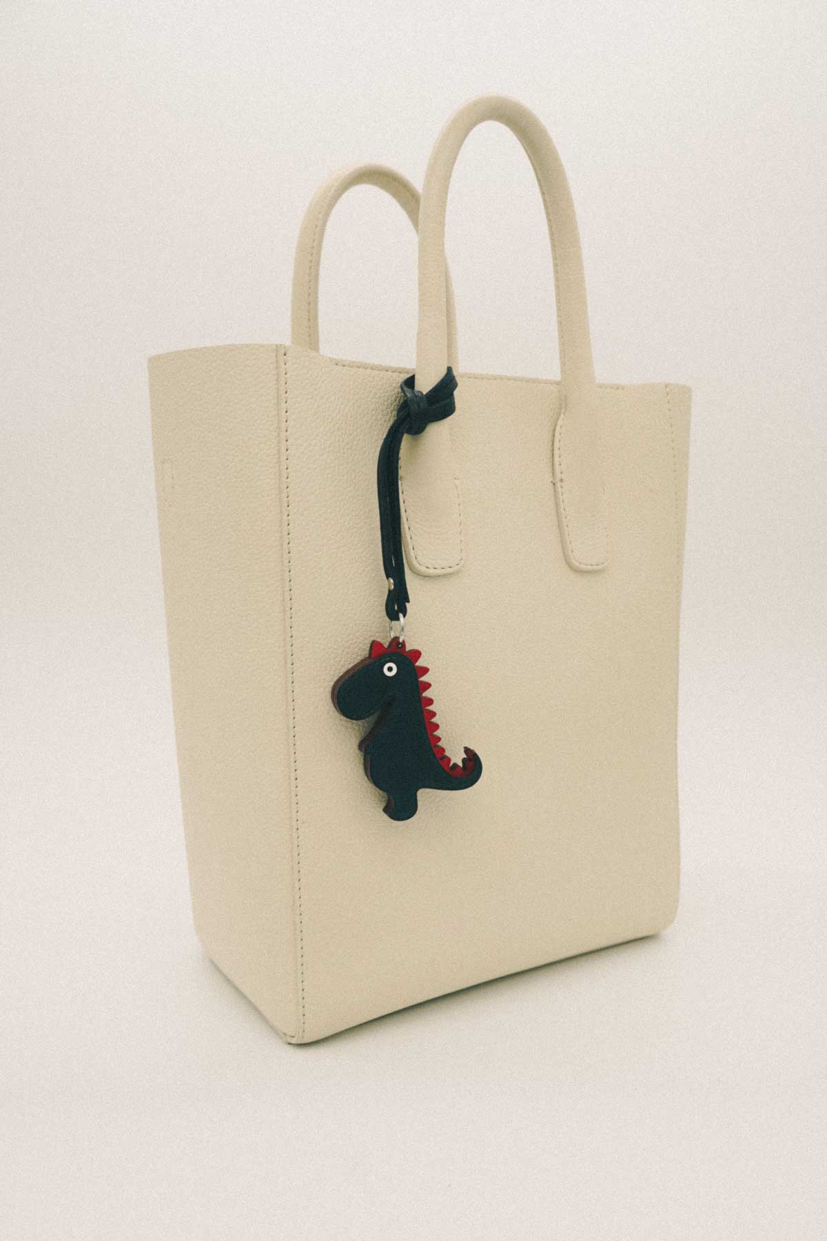 Beige tote bag with a dinosaur handmade leather bag charm on a white background