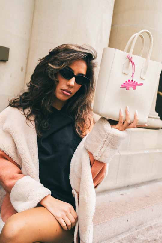 Woman sitting on a stone bench with a white tote bag featuring a pink handmade leather bag charm.