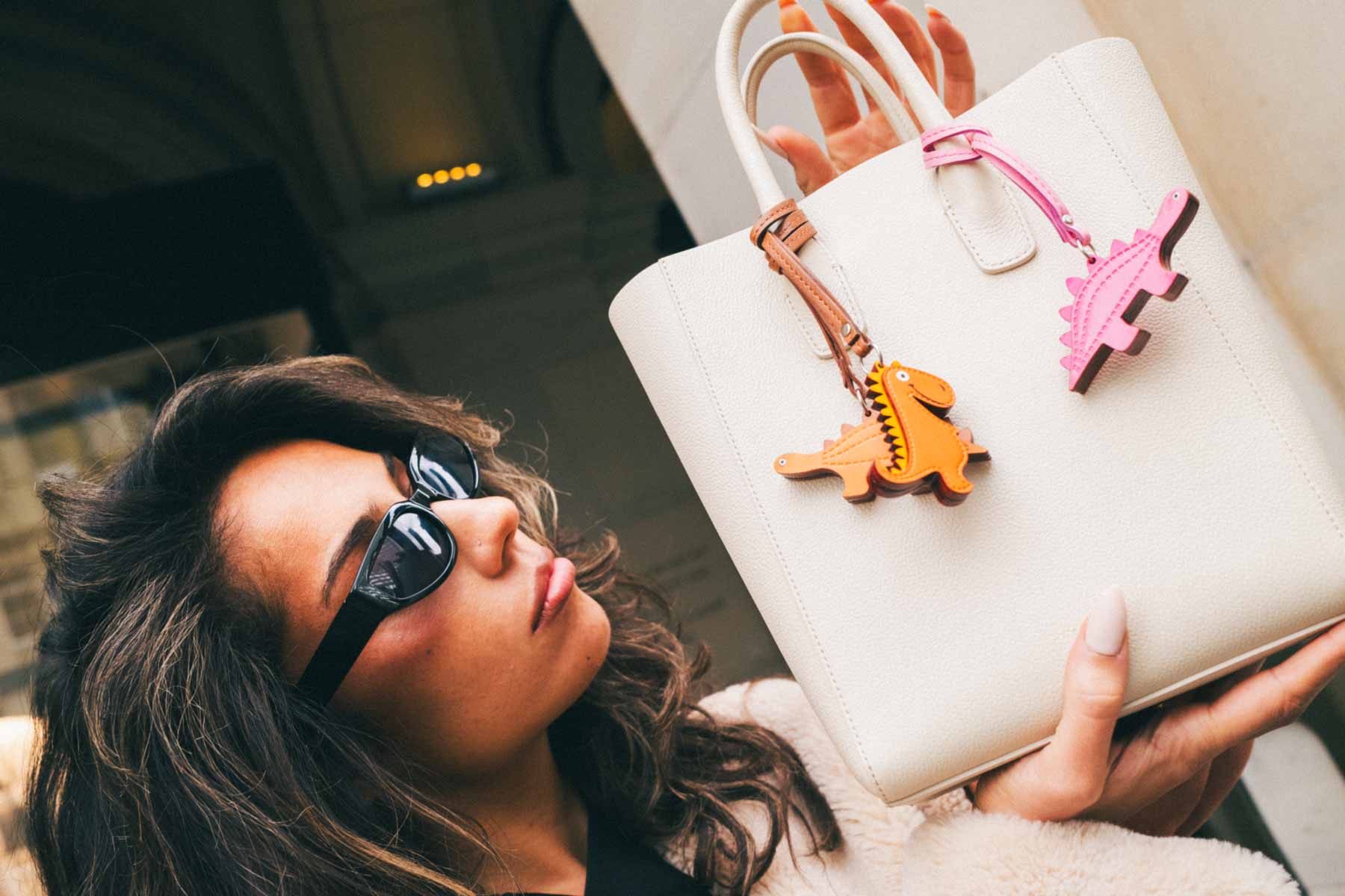 Woman holding a white handbag with colorful charms, wearing sunglasses.