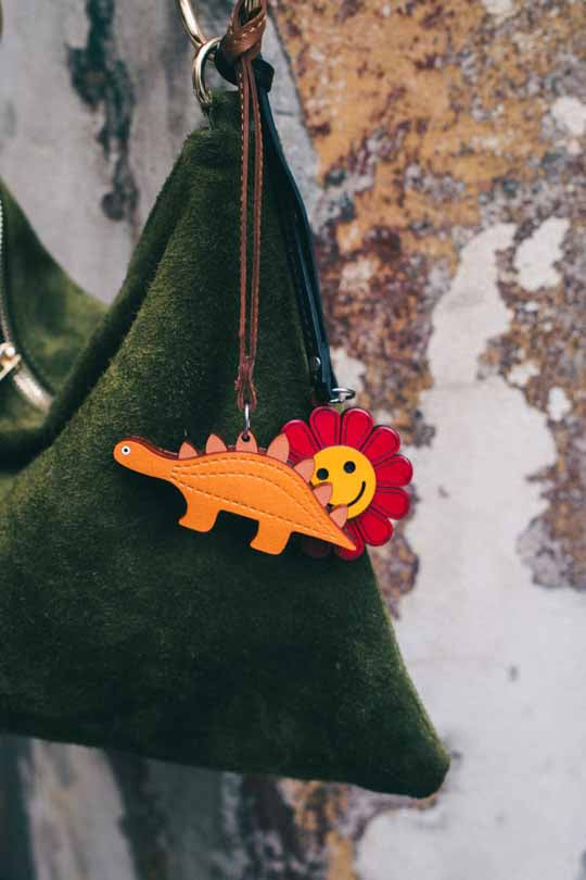 Keychain with orange dinosaur and red flower on a green bag against a textured background
