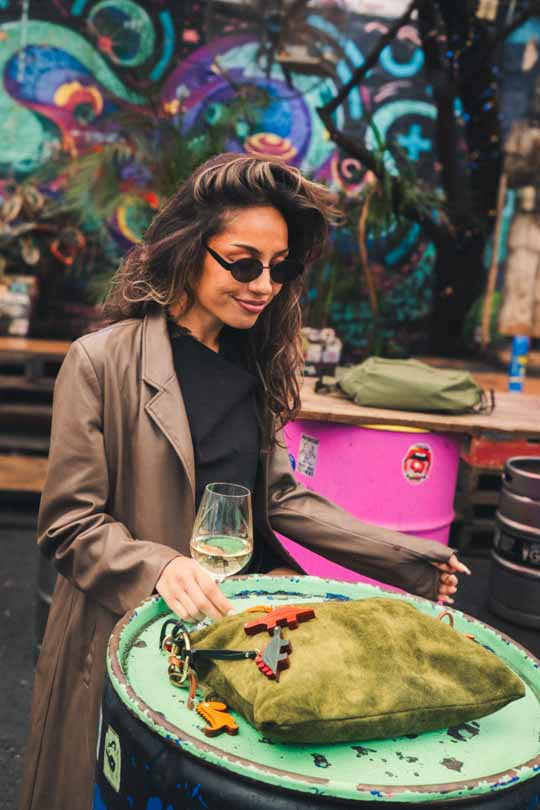 Woman in a cafe setting with a green bag and several handmade leather bag charms