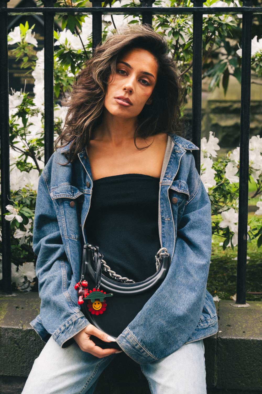 Woman wearing a denim jacket and black top with handmade leather bag charms attached to a black bag