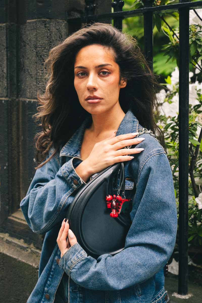 Woman holding a black bag with a red lobster and dark green dinosaur handmade leather bag charm