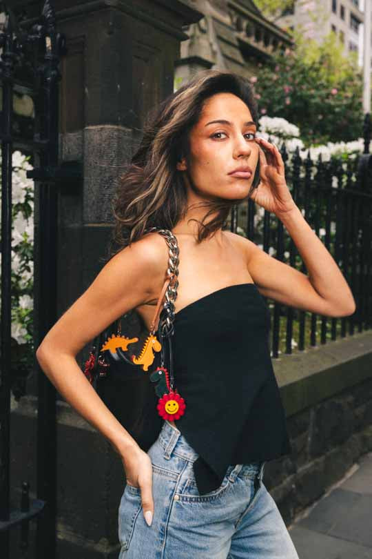 Woman wearing a black strapless top with colorful handmade leather bag charms and blue jeans, standing outdoors.