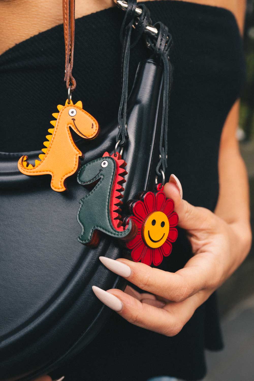 Person holding a black bag with dinosaur and flower keychains.