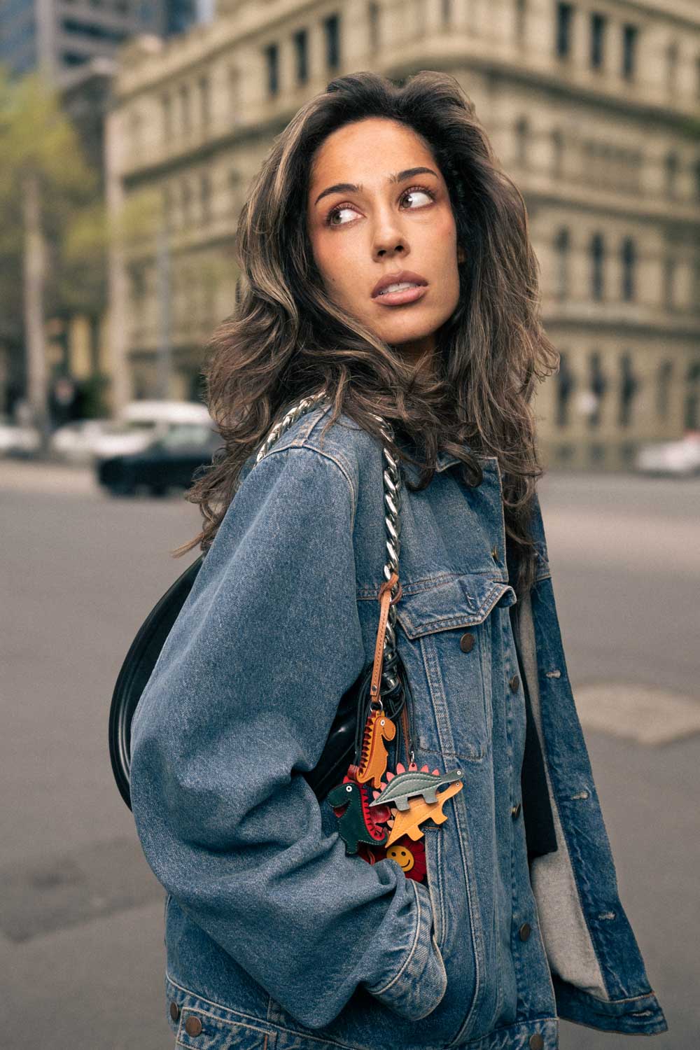 Woman wearing a denim jacket with dinosaur shaped handmade leather bag charms in an urban setting