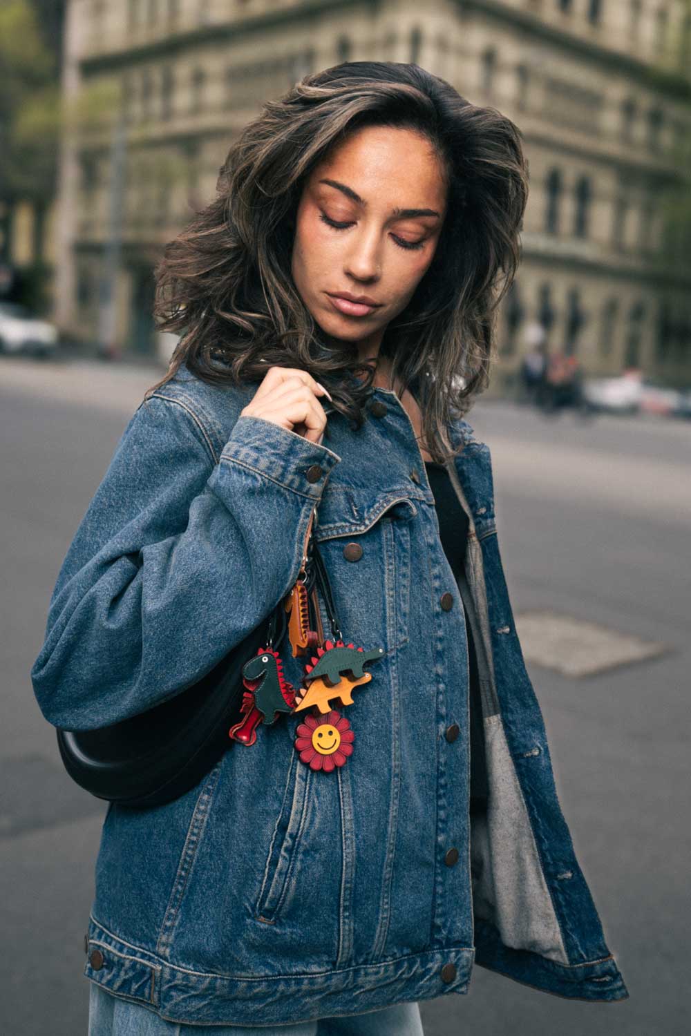 Woman wearing a denim jacket with colorful handmade leather bag charms on a city street