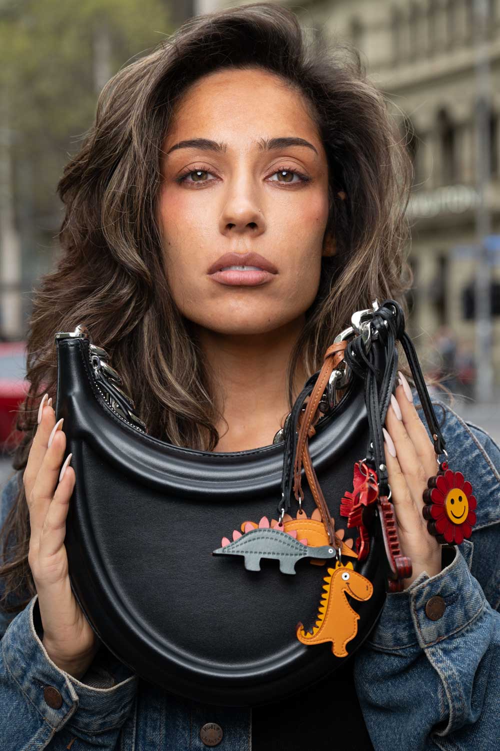 Woman holding a black handbag with colorful handmade leather bag charms in an urban setting
