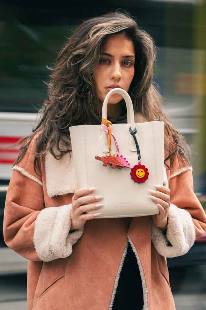 Woman holding a cream-colored handbag with colorful charms in an urban setting