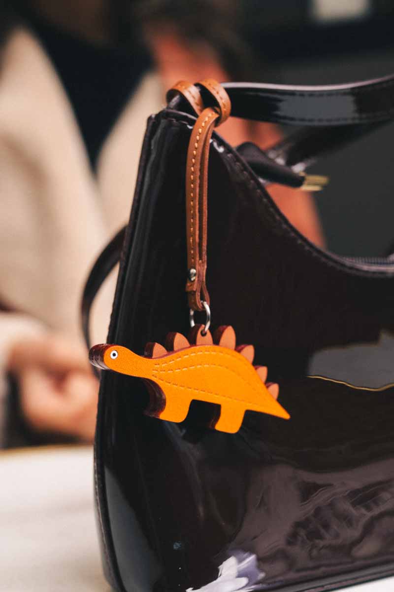 Brown handbag with a dinosaur-shaped handmade leather bag charm attached