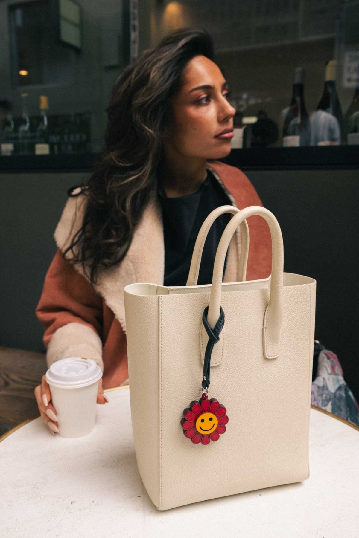 Woman holding a beige tote bag with a smiling flower handmade leather bag charm in an outdoor setting