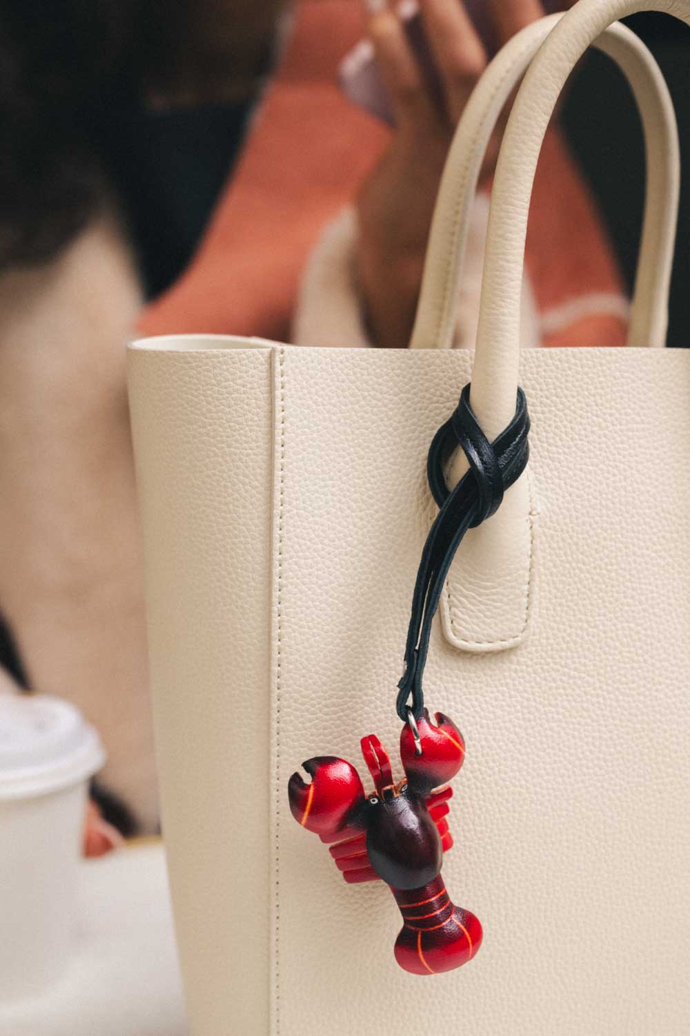 Beige handbag with a red lobster handmade leather bag charm against a blurred background