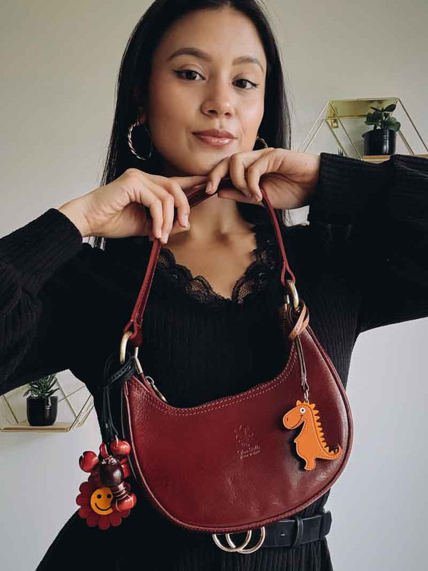 Woman holding a red handbag with dinosaur, lobster and flower charms against a neutral background