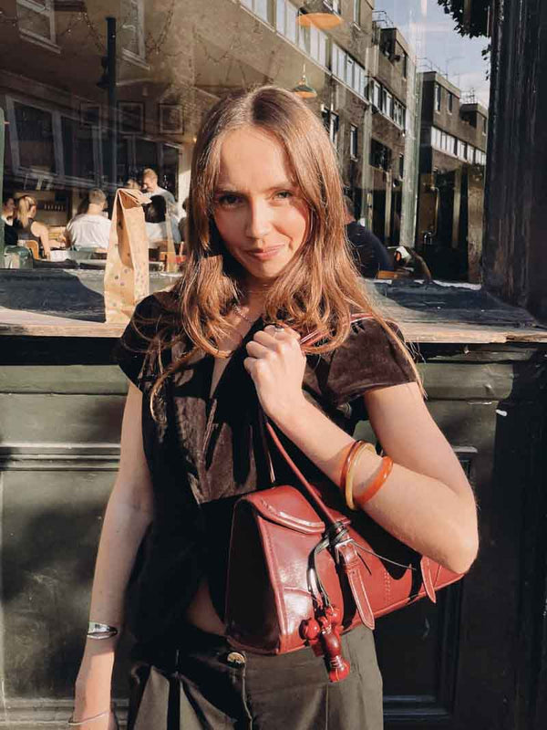 Woman holding a red handbag with a lobster bag charm in an urban setting